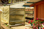 Open farm drying shelter with stacked racks and flowers near the entrance
